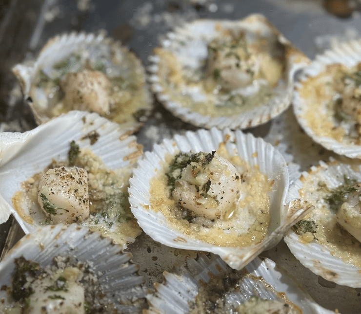 Scallops in shells with herbs and melted cheese on a pan.