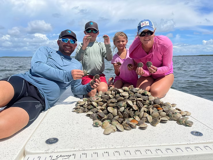 Four people on a boat displaying a large pile of clams.