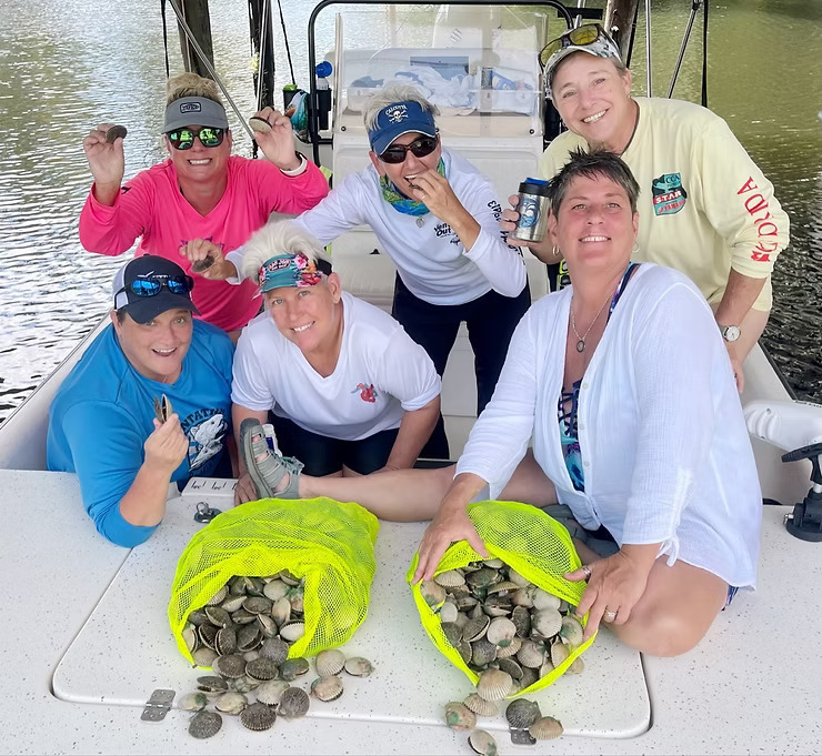 Group of six people on a boat with two bags of shells.