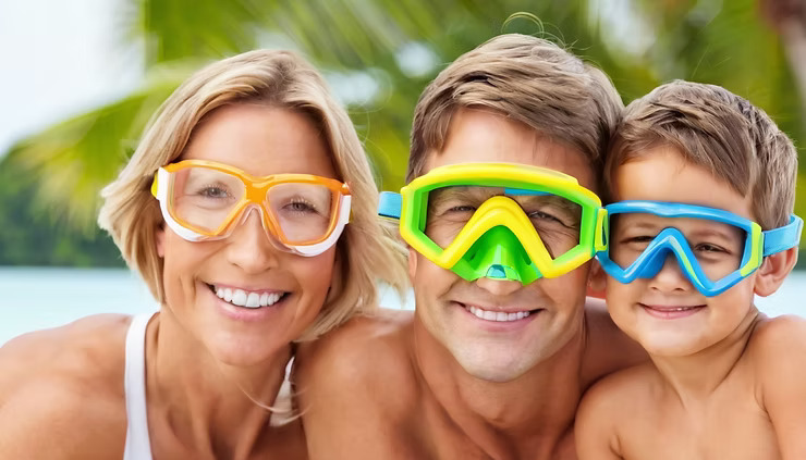 Family of three wearing snorkel masks, smiling in a tropical setting.