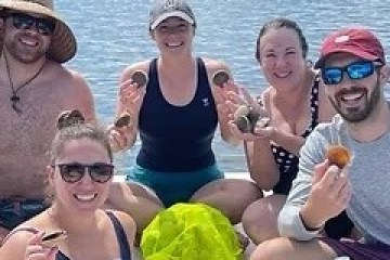 Group of five people on a boat holding seashells, smiling.