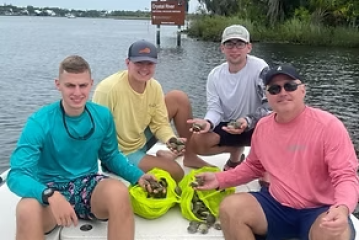 Four people on a boat holding bags of shells near water.