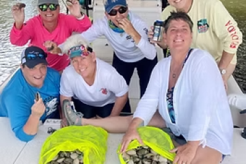 Group of six people smiling with two bags of collected clams on a boat.