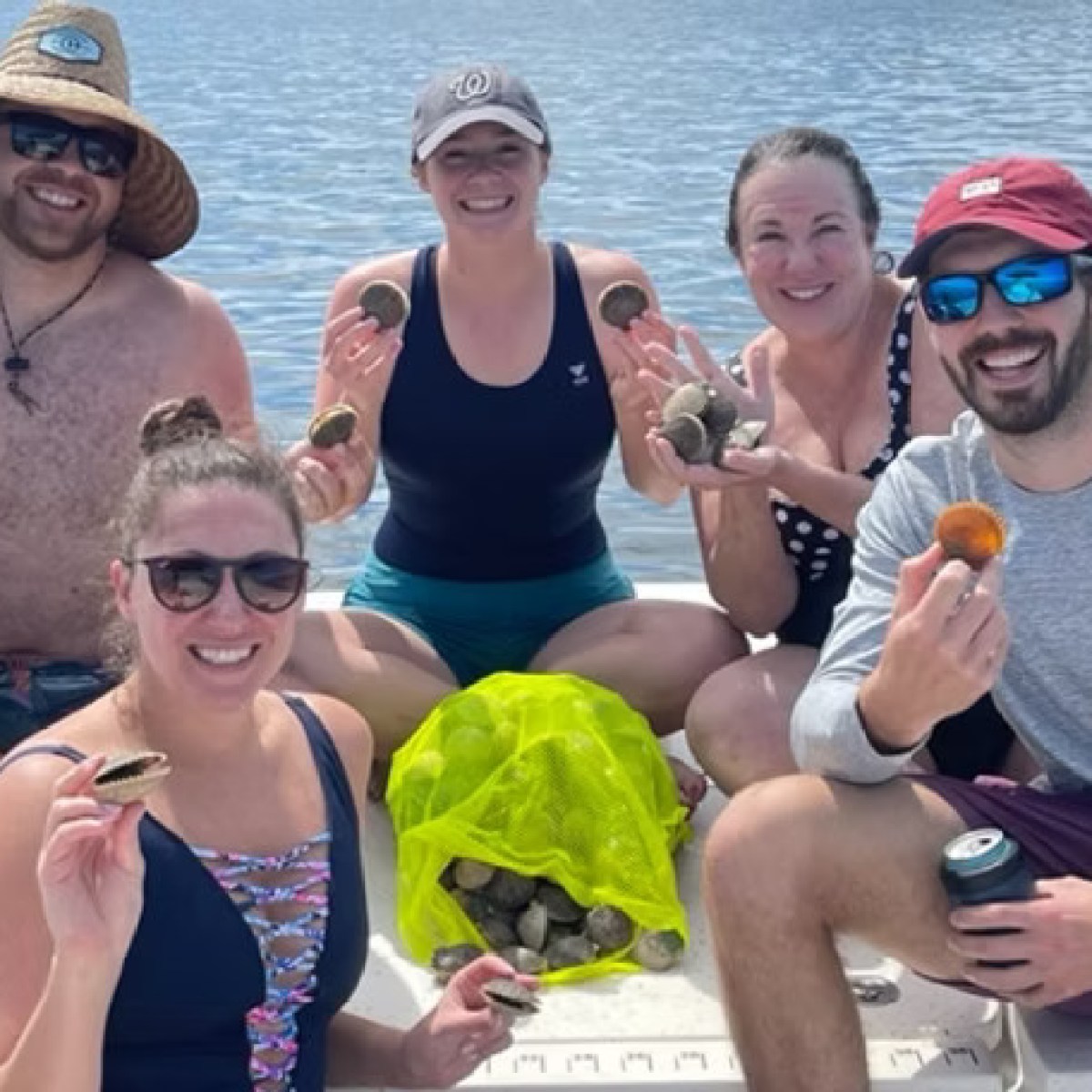 Group of five people on a boat holding scallops with a net bag of scallops.