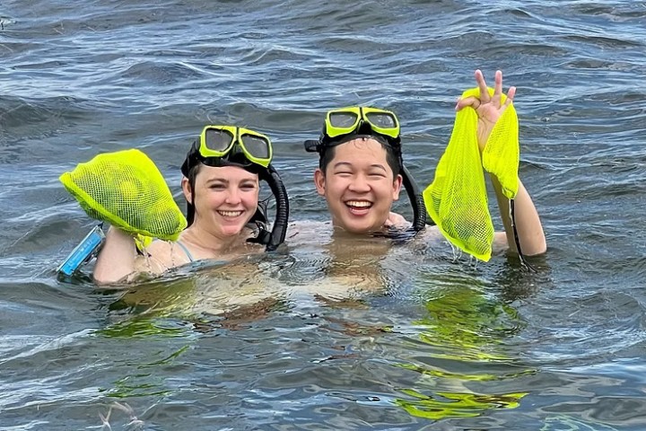 Two snorkelers in water holding yellow mesh bags and smiling.